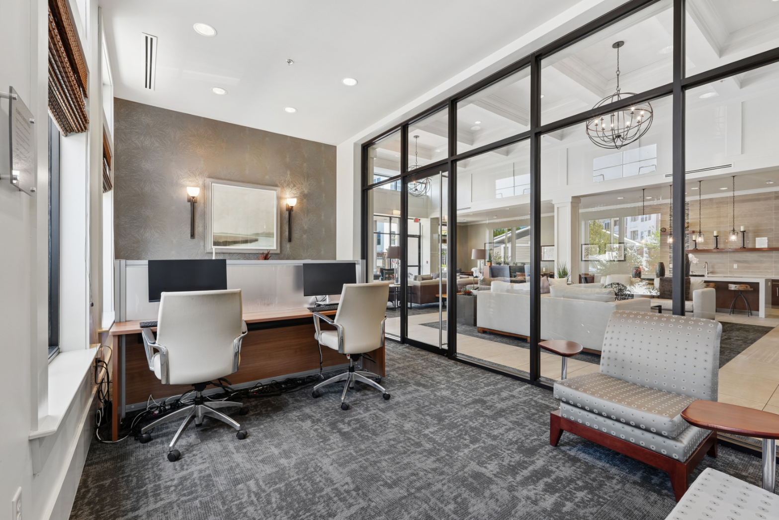 Business center with desks, office chairs, lounge seating, glass walls, and adjacent amenity space.