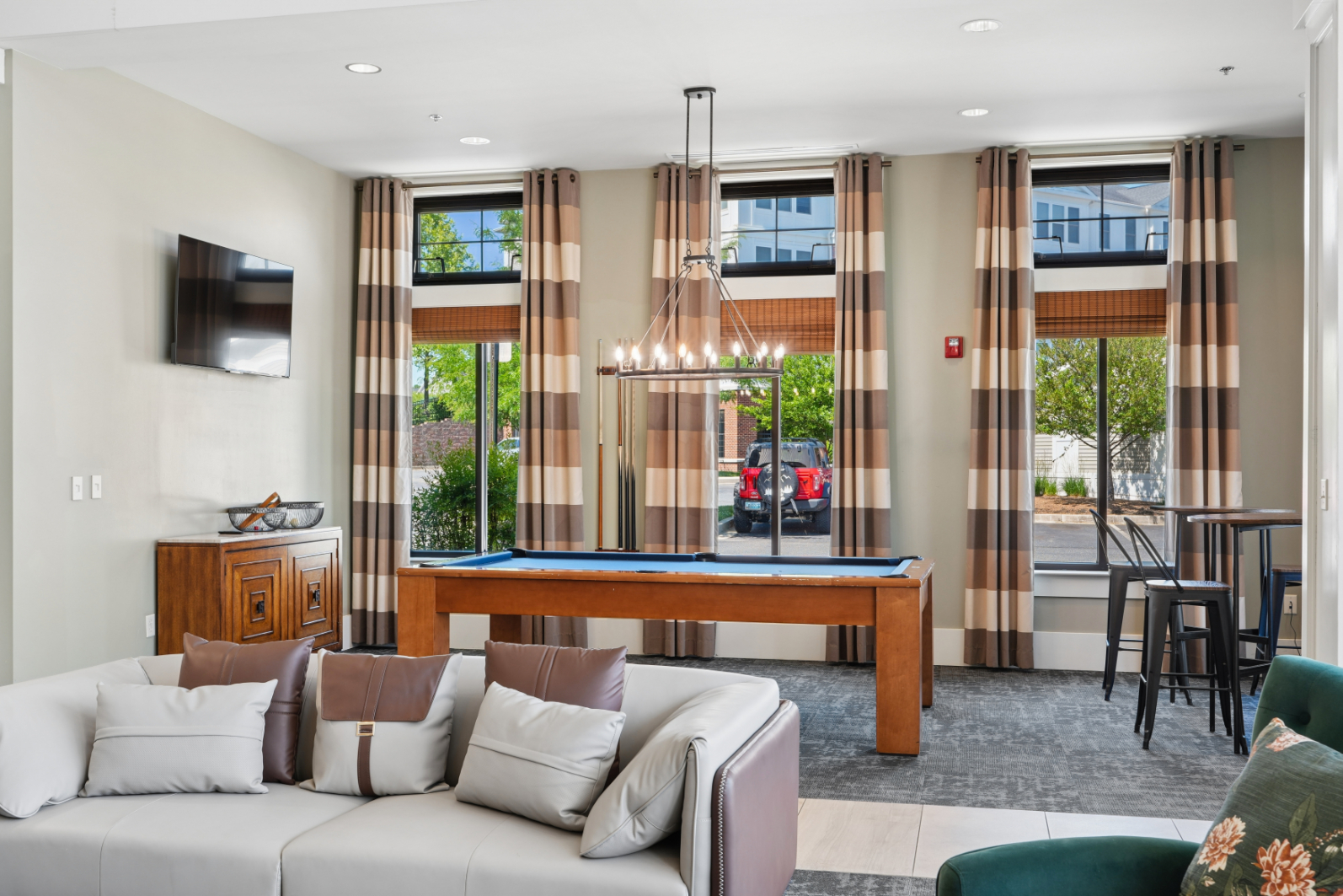 Clubroom seating area with billiards table, wall-mounted TV, large windows, and lounge furniture.