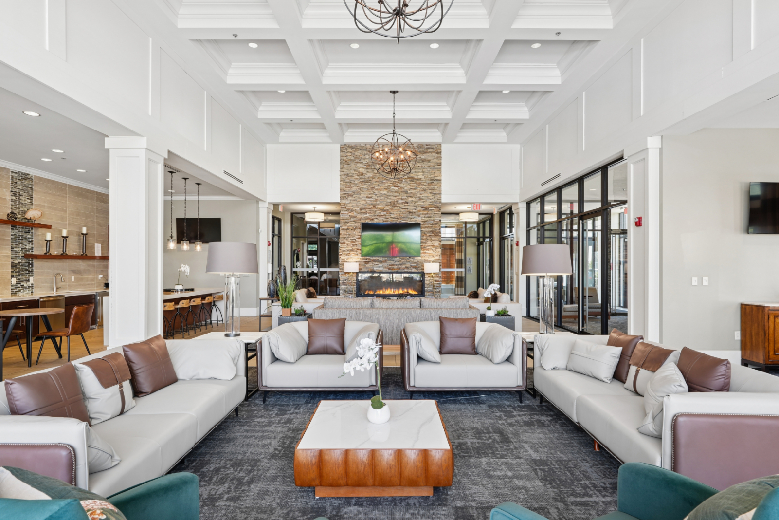 Clubroom lounge with sofas, fireplace, wall-mounted TV, bar seating, and coffered ceiling.