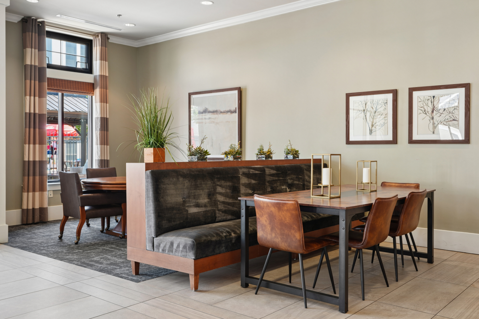 Clubroom table seating with upholstered chairs, wood table, tall windows, and framed wall art.