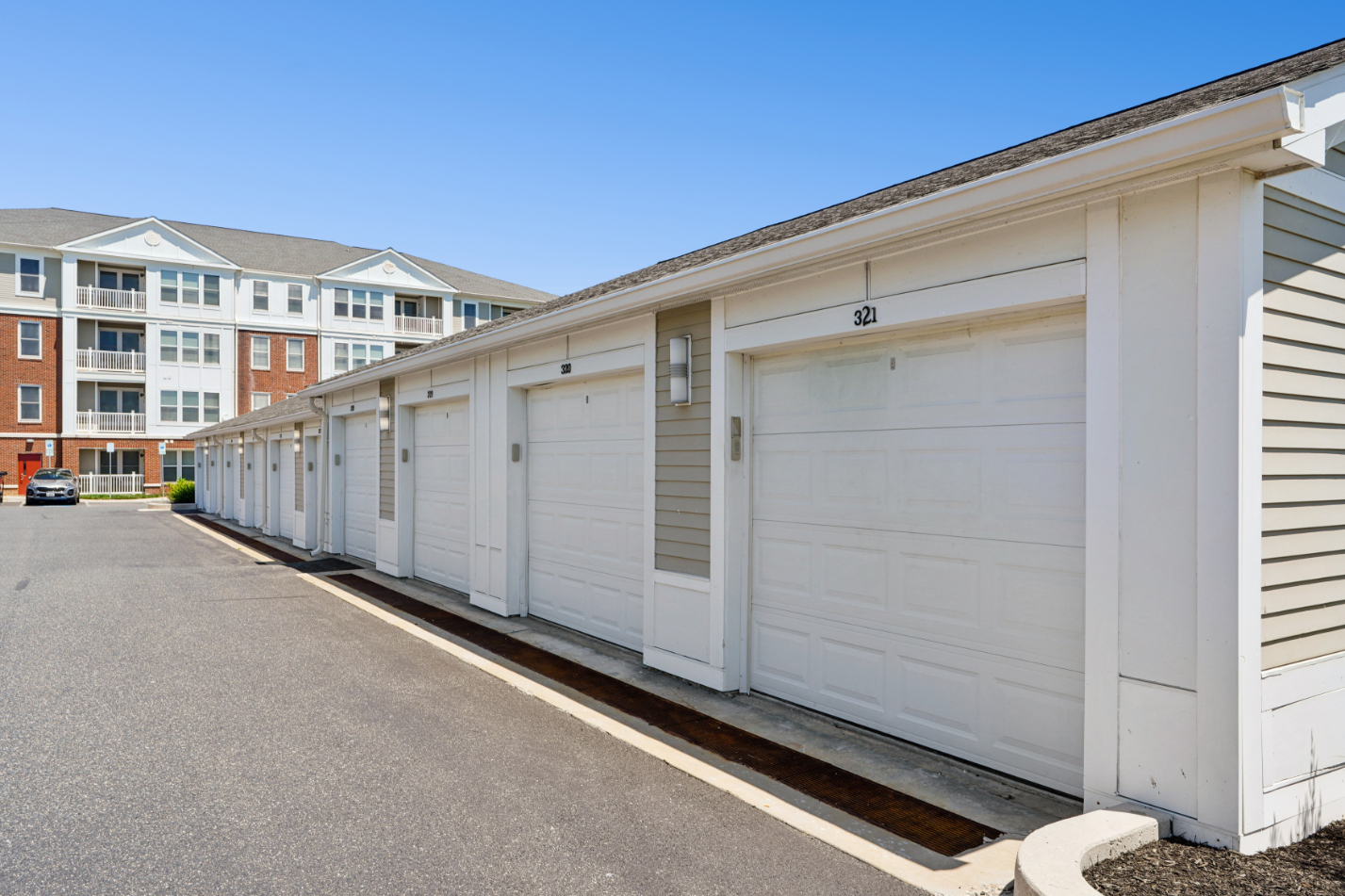 Row of detached white garages beside an apartment building and paved drive.