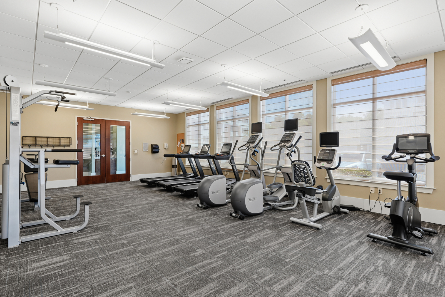 Fitness center with treadmills, ellipticals, strength machine, and windows along the wall.