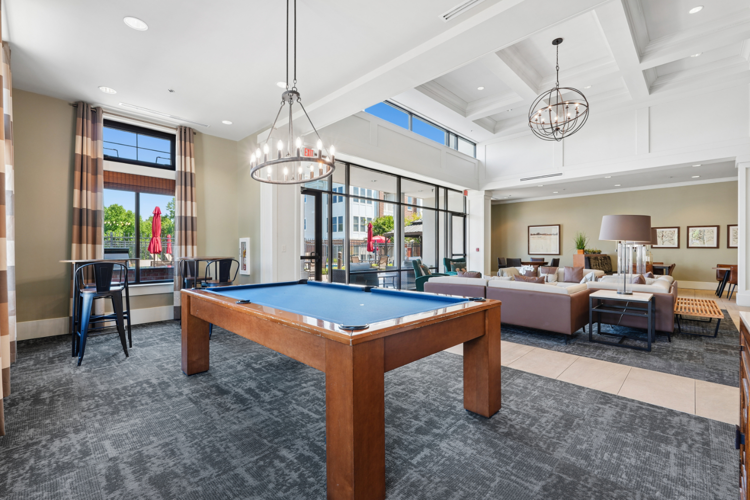 Billiards table in a clubroom with sofas, tall windows, pendant lighting, and access to the outdoor pool area.