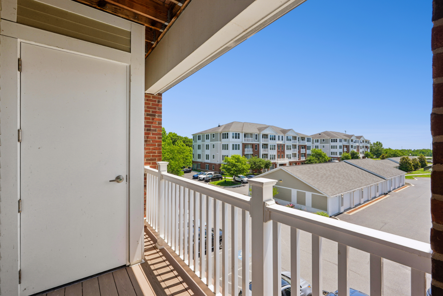 Apartment balcony with white railing and a view of nearby buildings and garages under a blue sky.