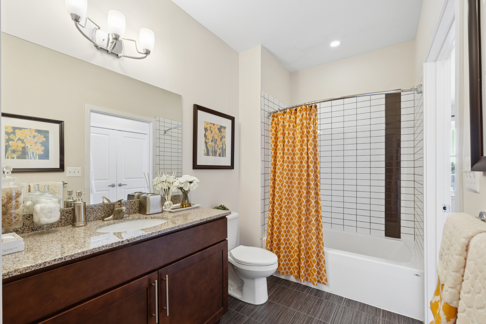 Apartment bathroom with wood vanity, granite-style countertop, toilet, bathtub, and patterned shower curtain.