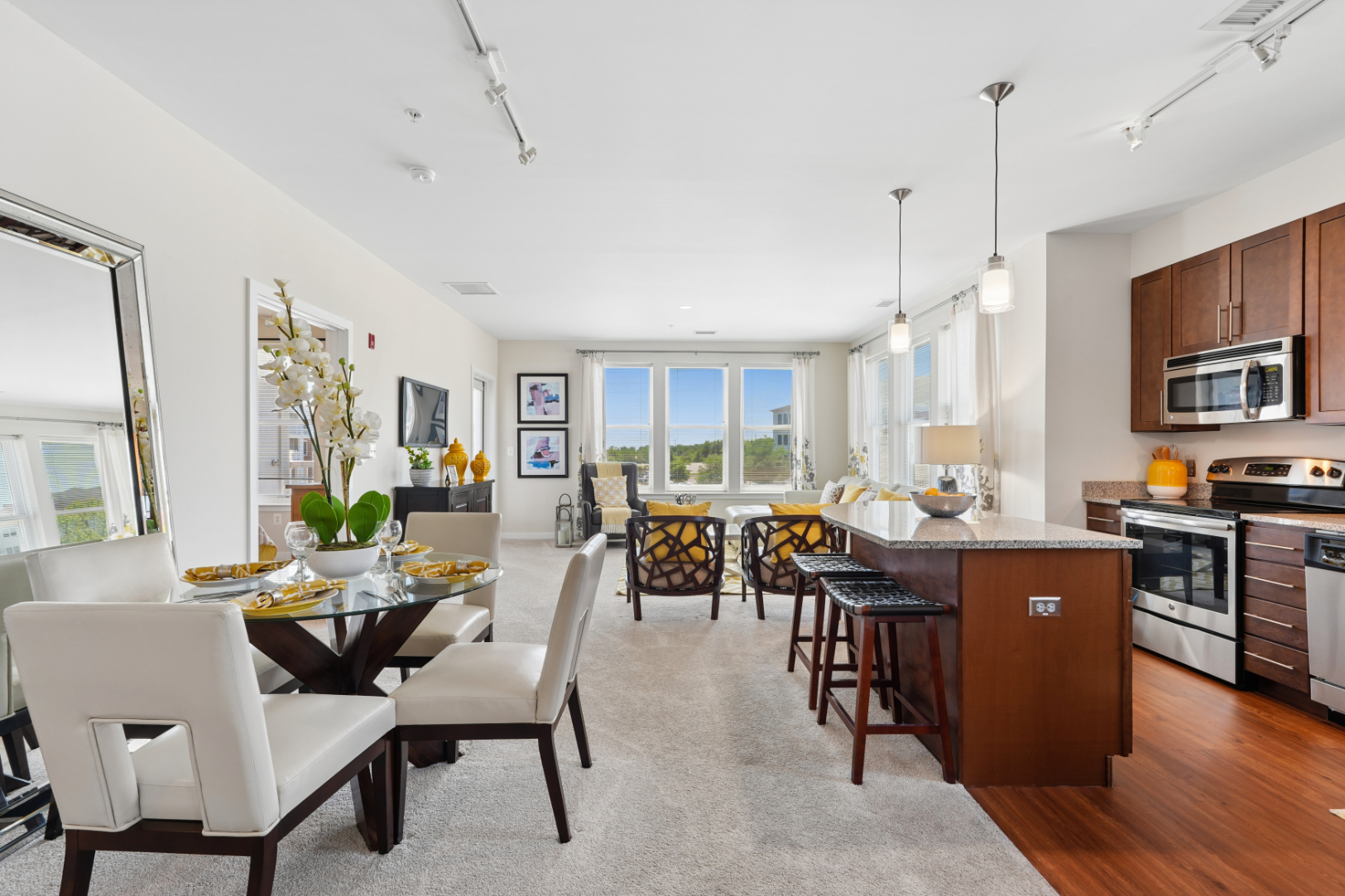 Open apartment kitchen and living area with wood cabinetry, island seating, dining table, and large windows.