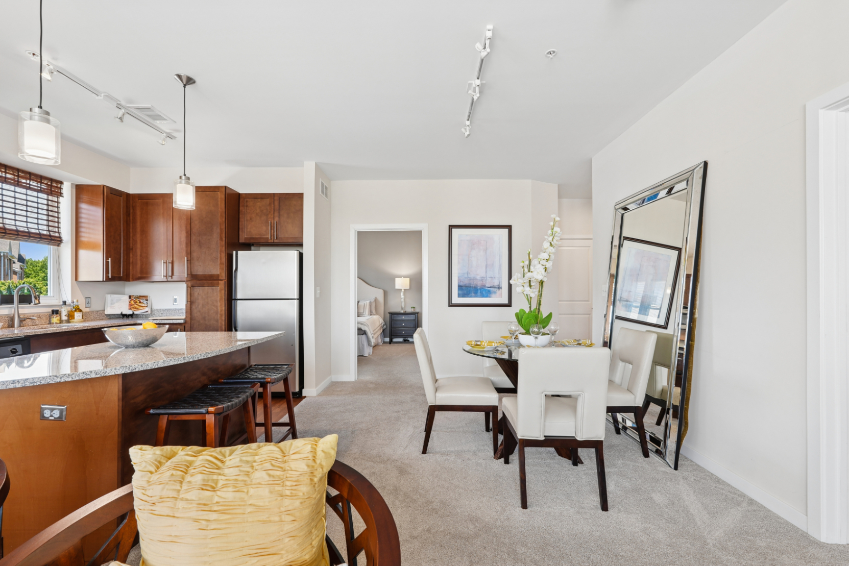Dining area beside an apartment kitchen island with a living room and bedroom doorway visible beyond.