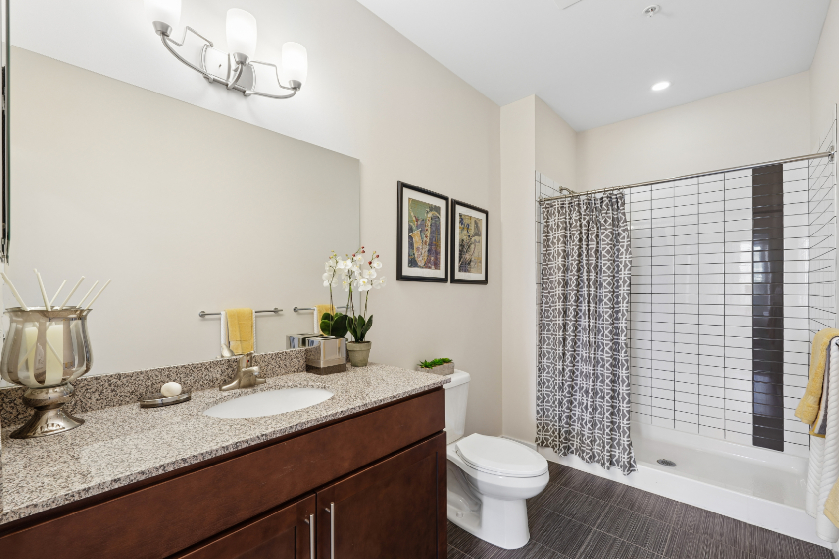 Primary bathroom with long vanity, wood cabinets, granite-style countertop, toilet, tub, and tile surround.