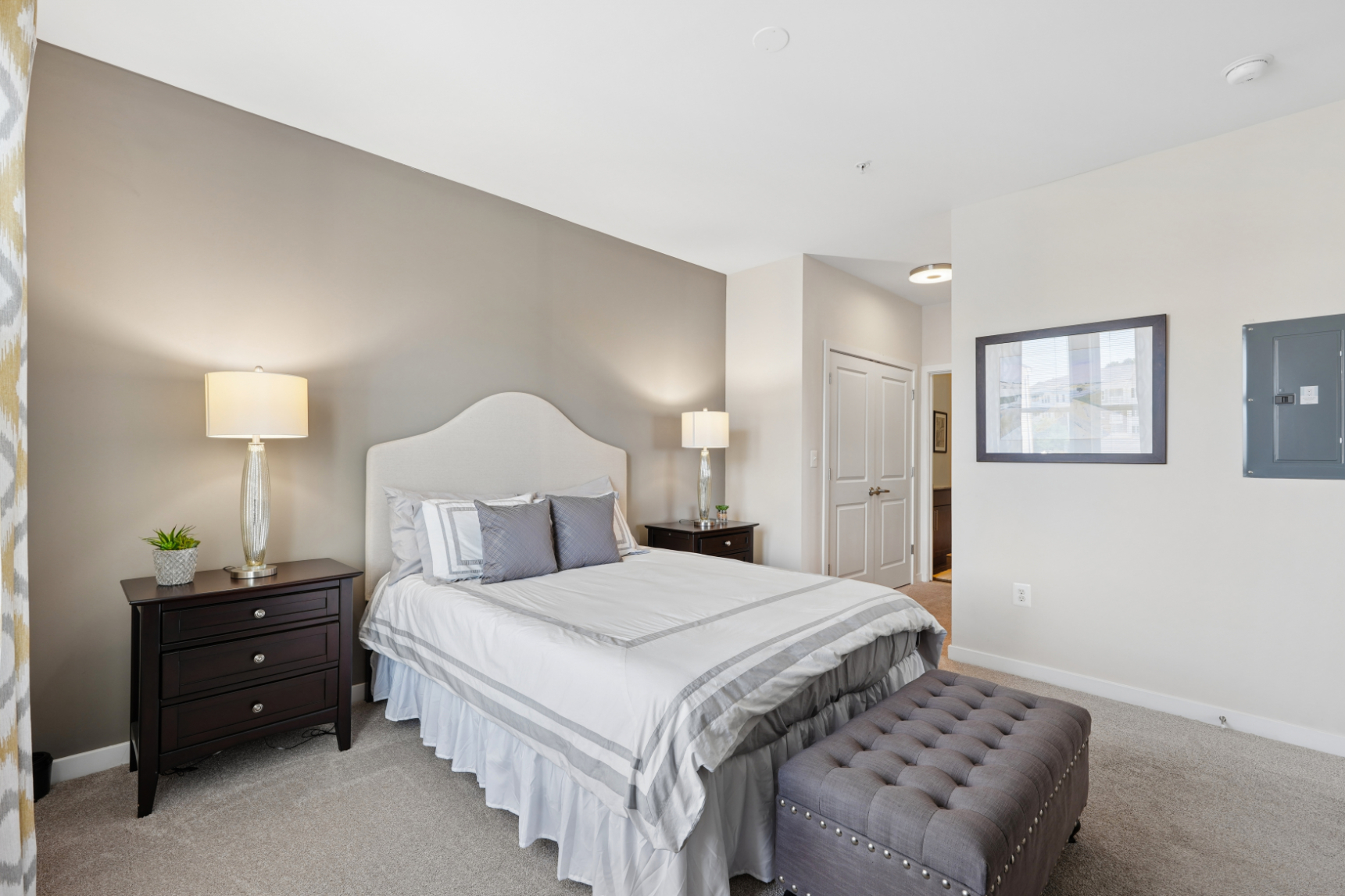 Primary bedroom with bed, nightstands, bench, gray accent wall, and open doorway to bathroom or closet.